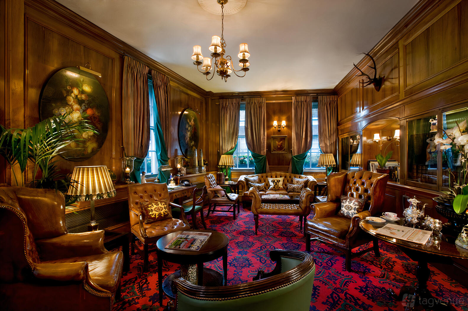 An event space in a hotel with wood-paneled walls, leather armchairs, chandeliers, and patterned carpet at The Chesterfield Mayfair
