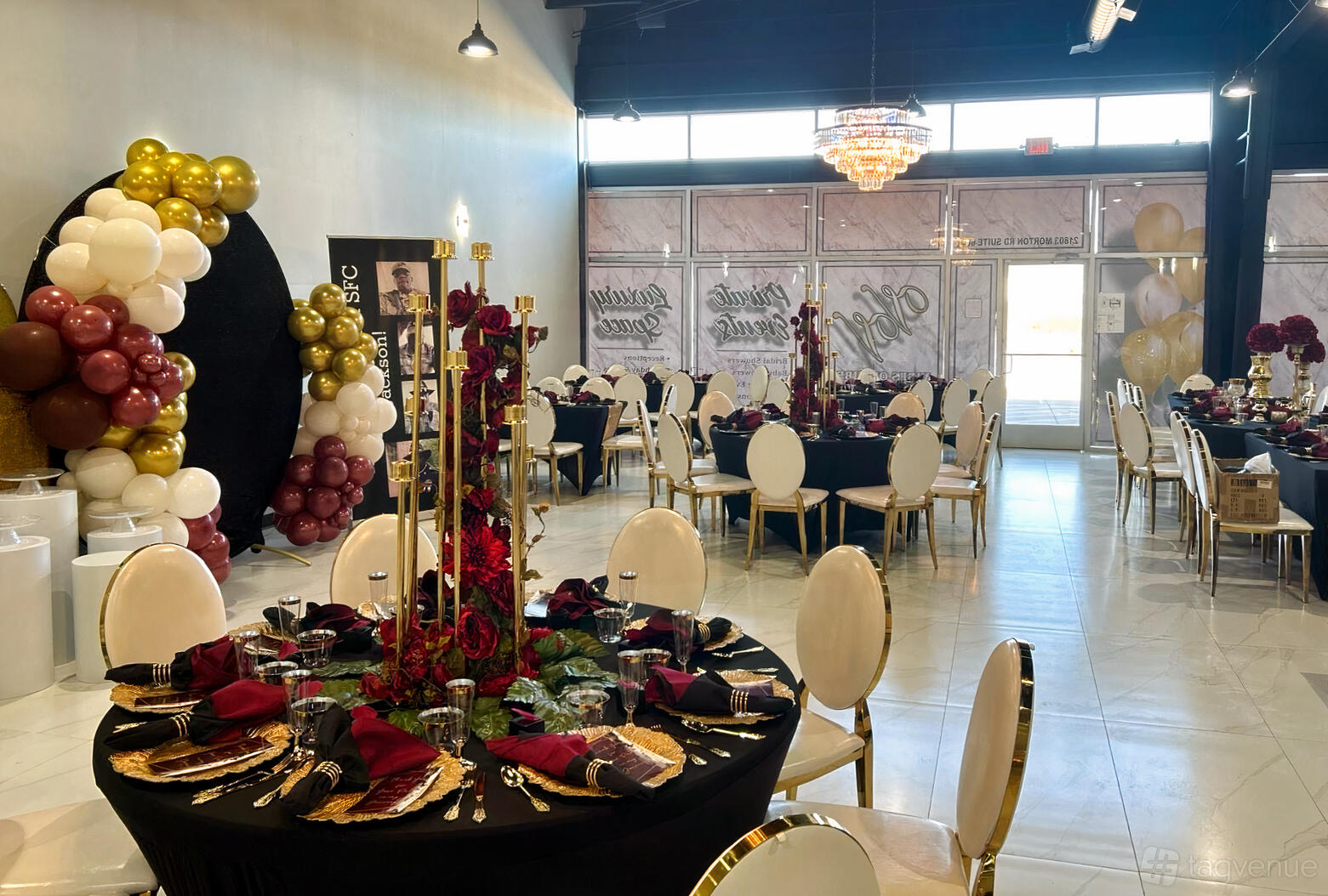An event venue with round tables dressed in black linens, gold chairs, and a balloon arch at Vibes on Vibes.