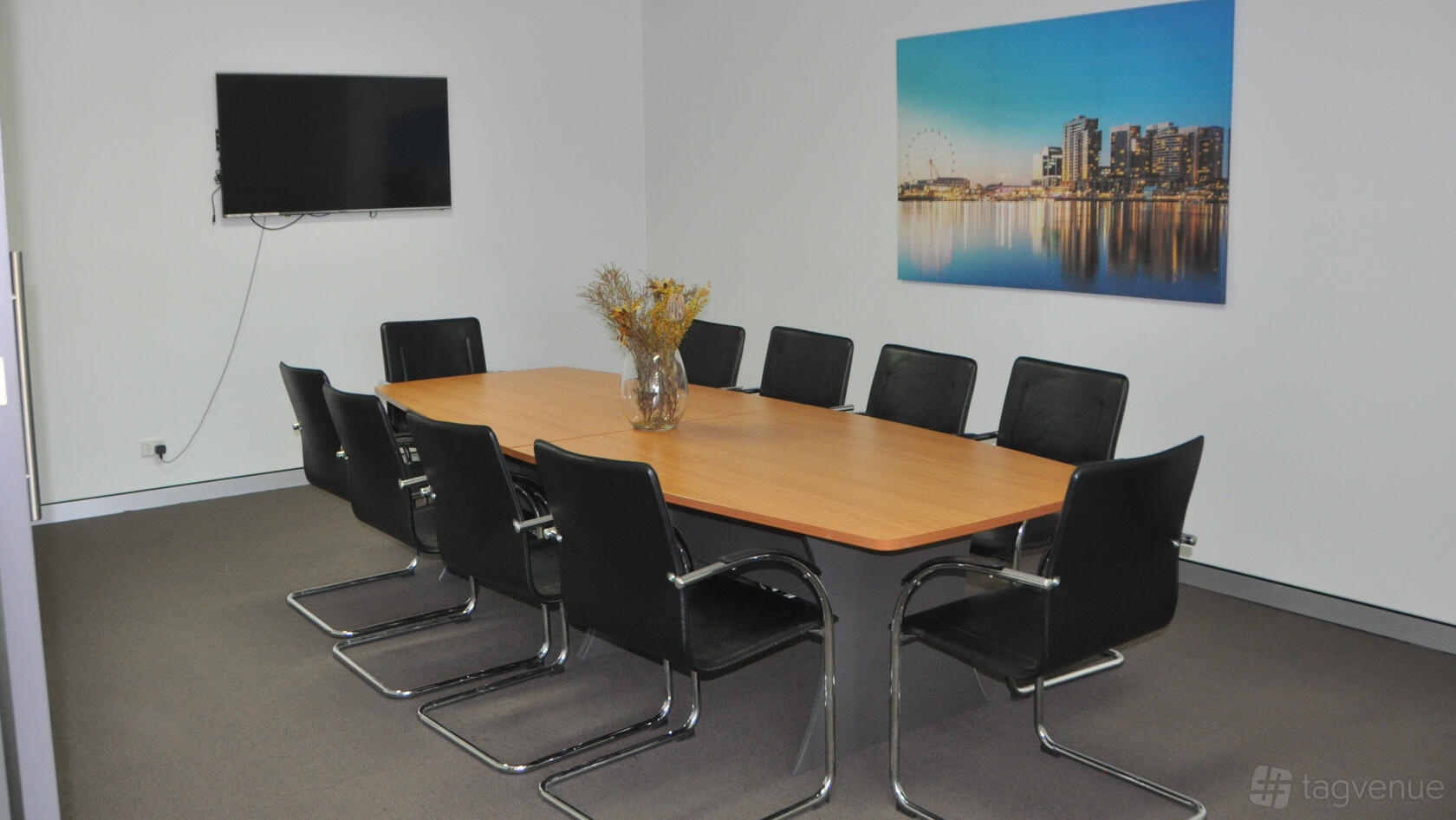 A boardroom with a rectangular wooden table, black chairs, wall-mounted TV, and cityscape artwork at Local Inspections.