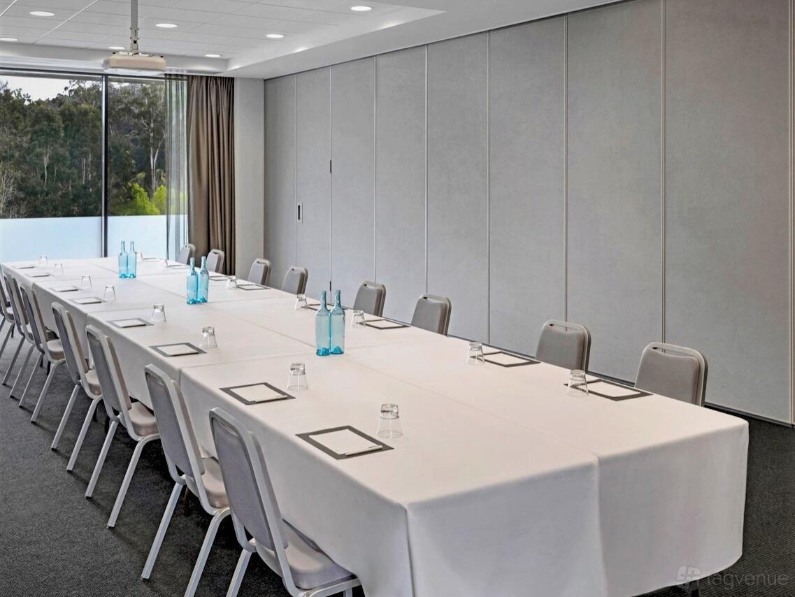 A meeting room with large windows, long rectangular tables, grey chairs, and notepads at Peppers Marysville.