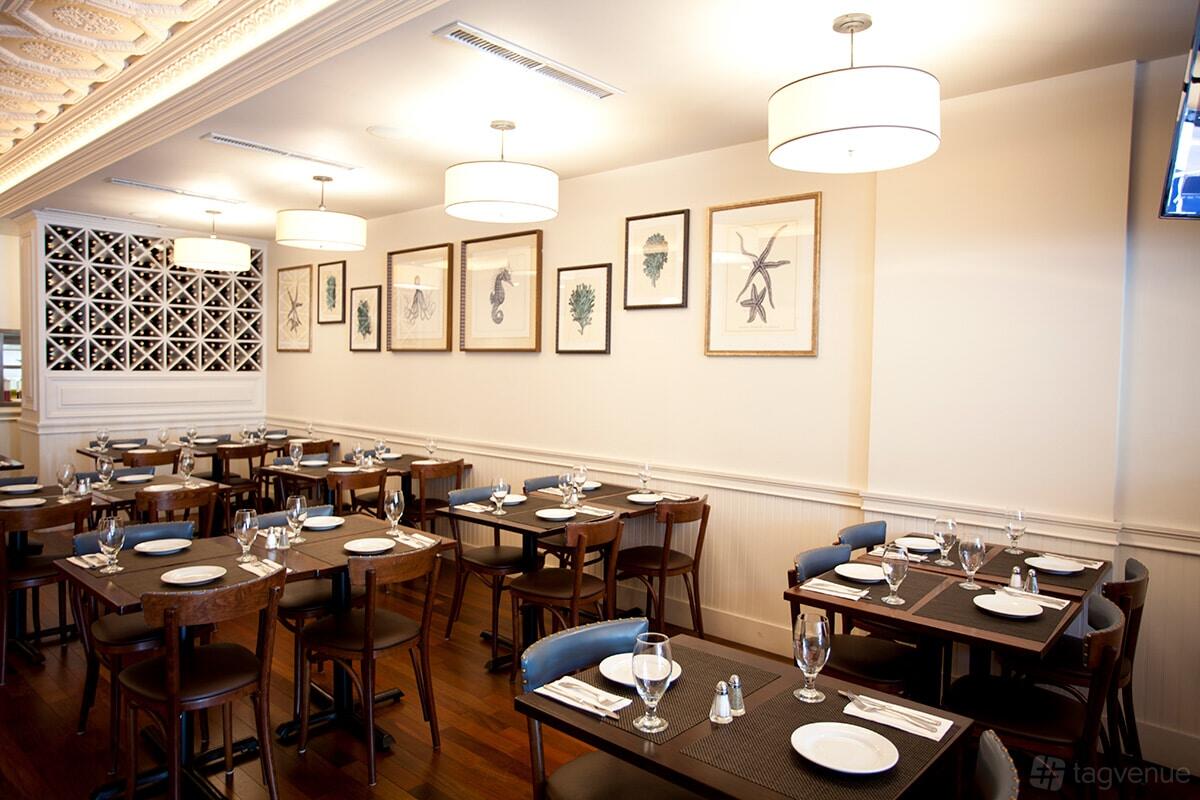 An event space in a restaurant with wooden tables, framed wall art, and ceiling lamps at Psari Restaurant.
