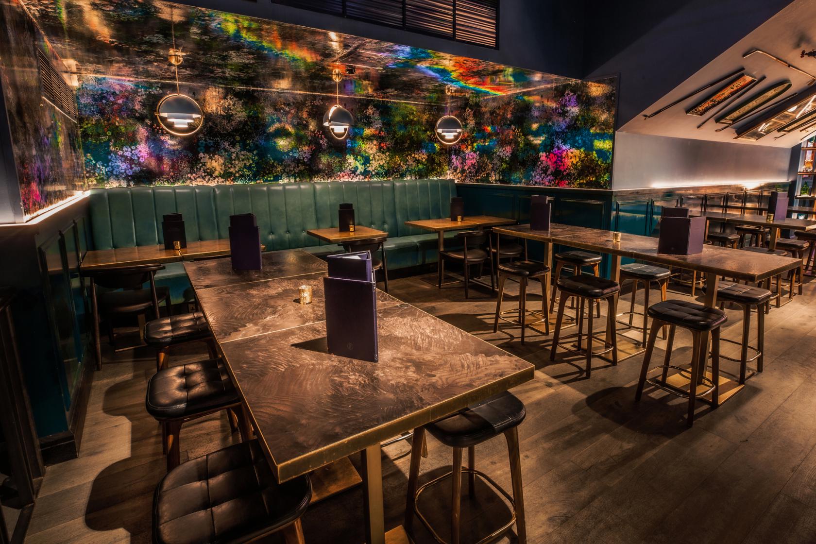 An event venue with teal leather banquette seating, wood tables, and colorful mirrored wall at Puttshack Bank.