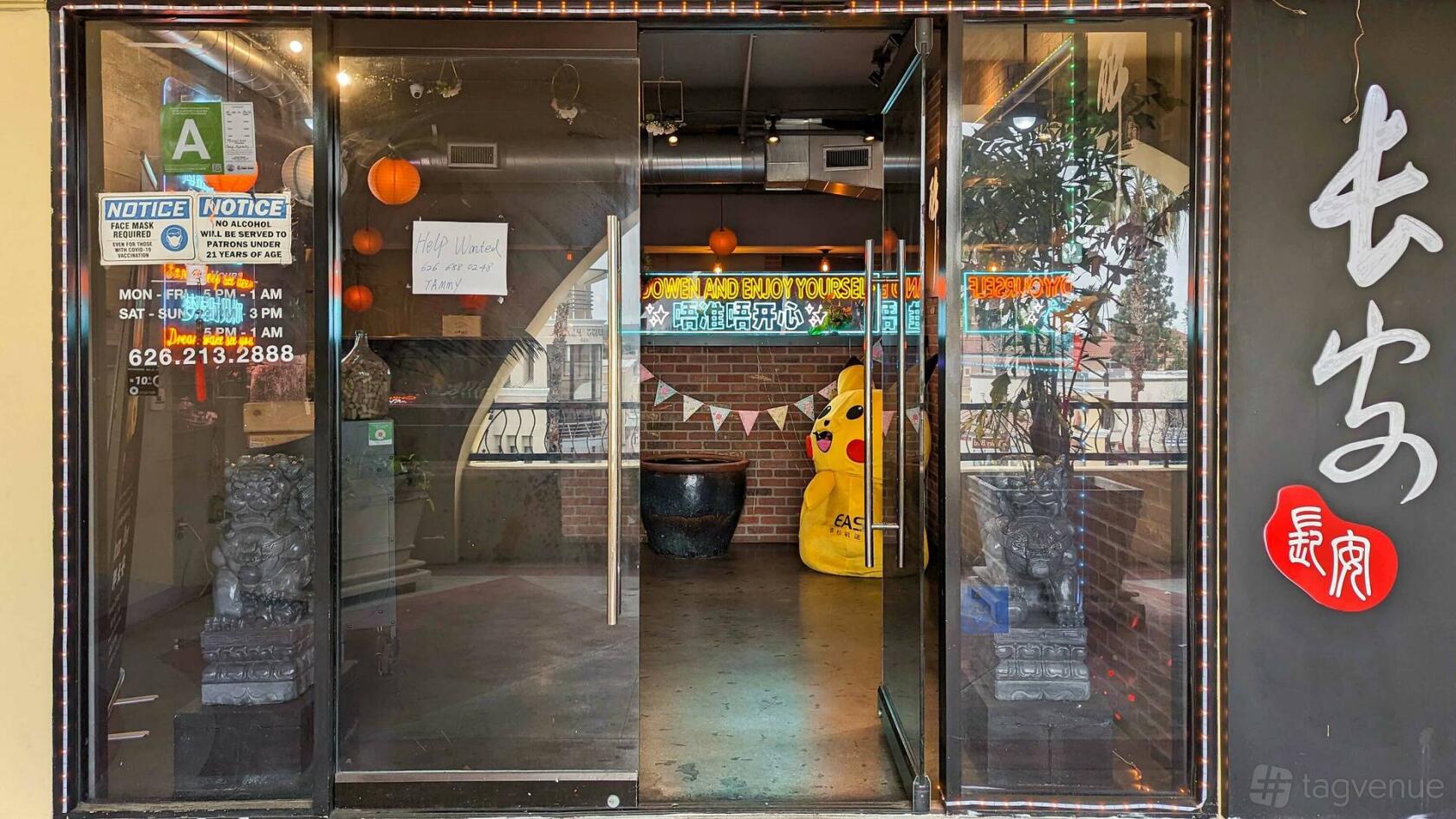 A restaurant entryway with glass doors, red lanterns, brick walls, and a large yellow mascot at Tang Dynasty.