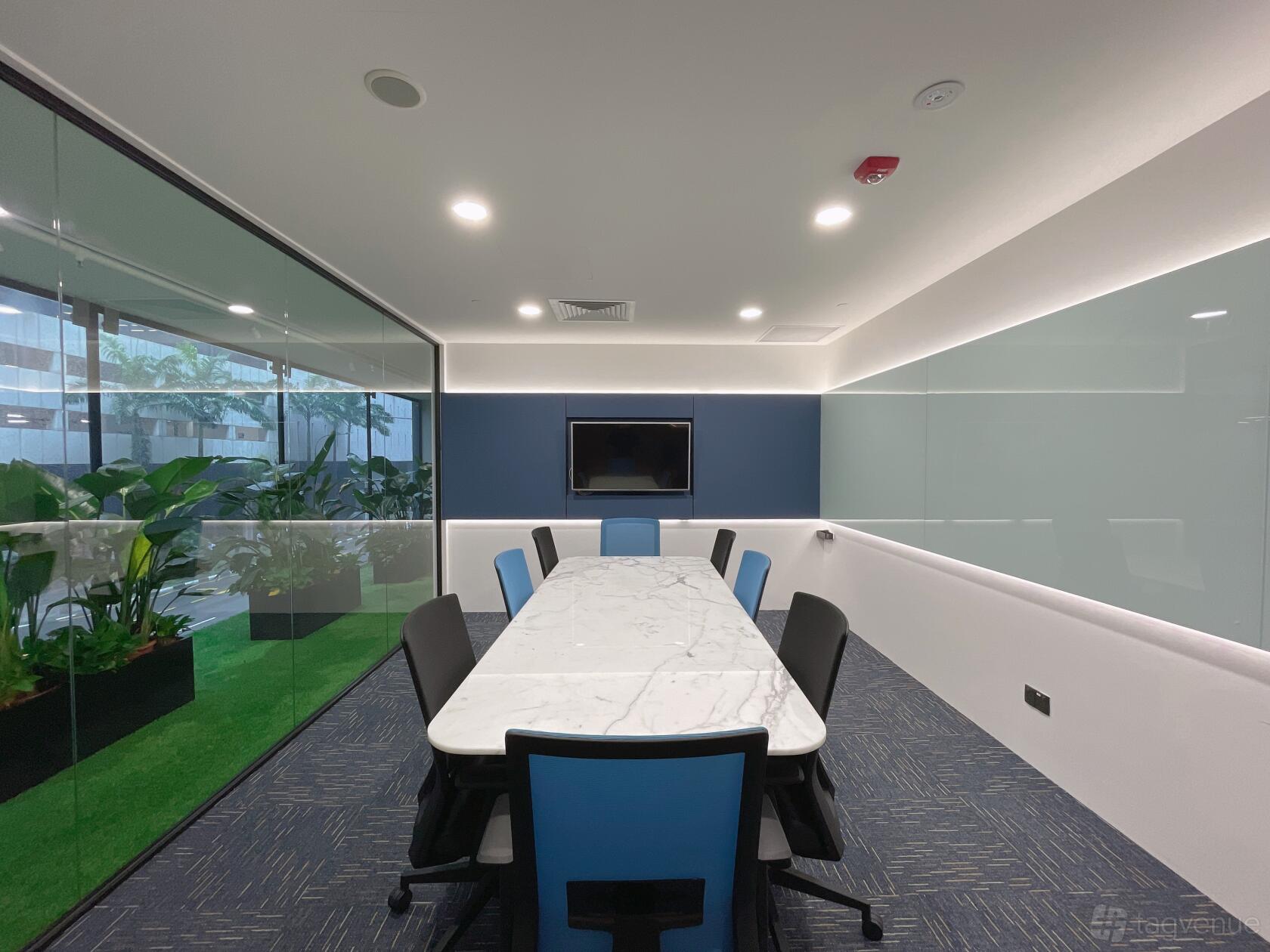 A meeting room with a long marble table, blue chairs, glass walls, and a wall-mounted screen at Le Space.