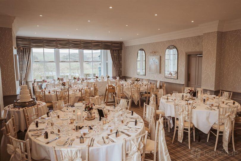A hotel event space with large windows, round tables with white linens, and elegant decor at The Devonshire Fell Hotel & Restaurant.