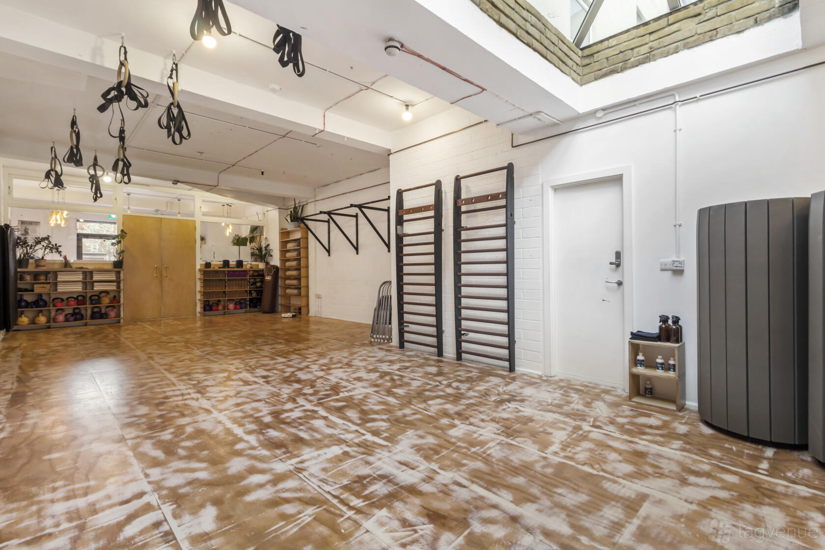 A yoga studio with wall-mounted bars, wooden floors, skylight, and shelves with kettlebells at Waking Dreams.
