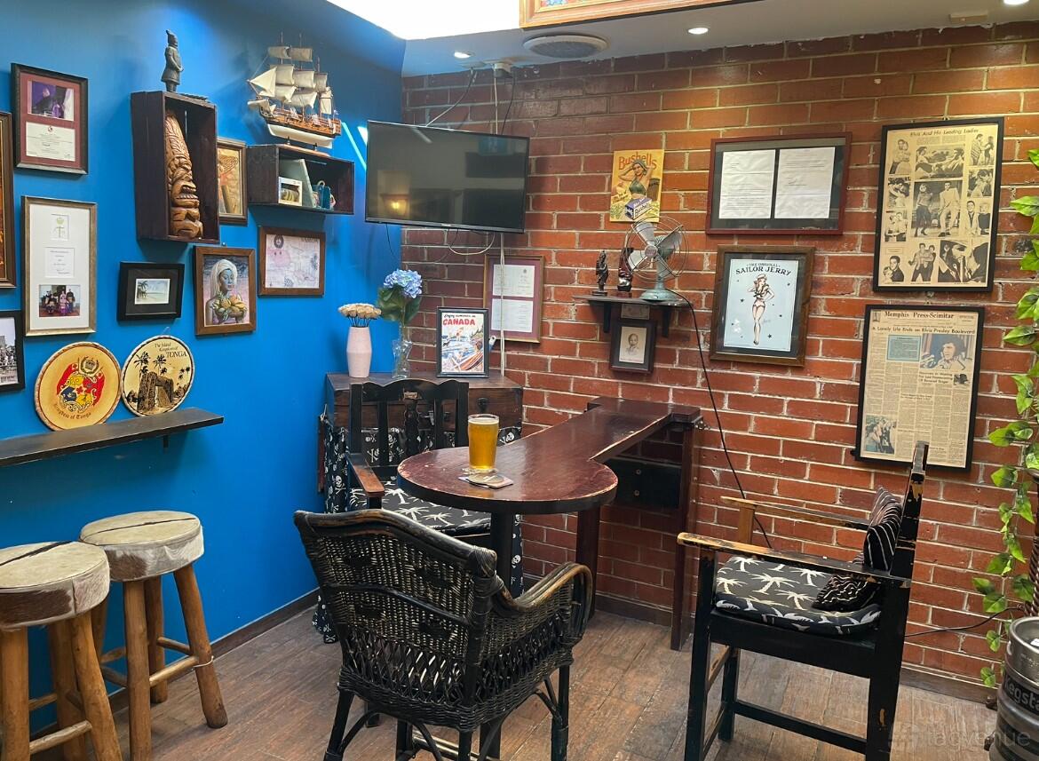 A dining room in a bar with exposed brick walls, eclectic framed art, wicker chairs, and a small round table at The King of Tonga.