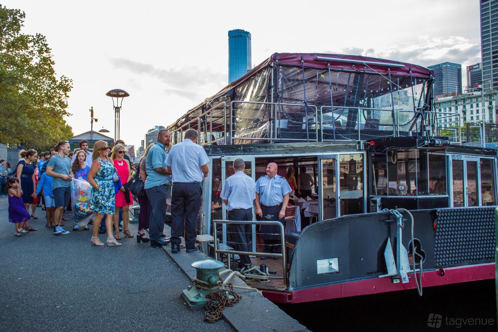 A docked boat with guests boarding near glass windows and a covered upper deck at Spirit Of Melbourne Cruising Restaurant.