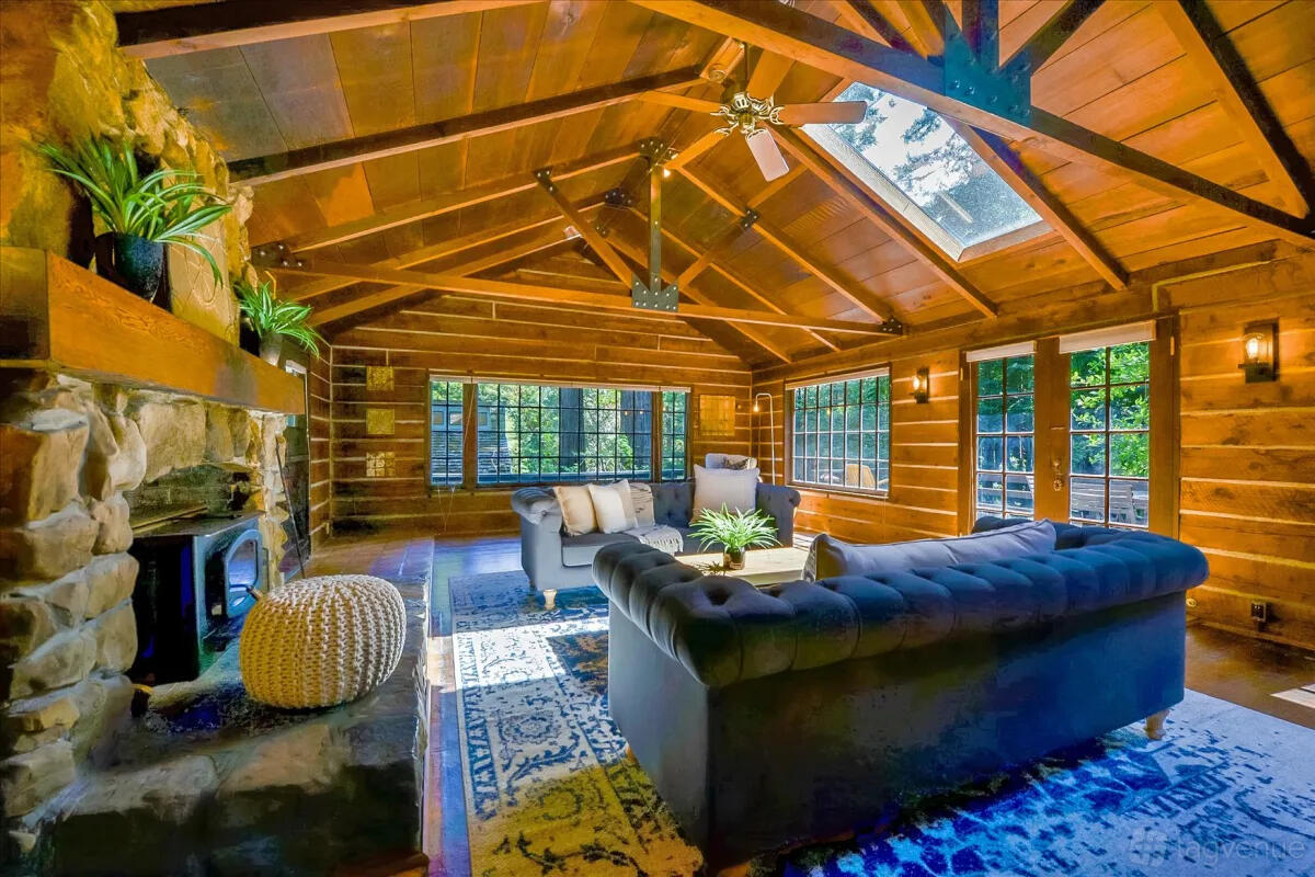 A log-cabin apartment with exposed wood beams, stone fireplace, large windows, and a skylight at Log-Cabin Home Retreat.