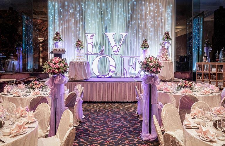 A hotel lounge with round banquet tables, floral centerpieces, stage decor, and draped lights at Furama RiverFront.