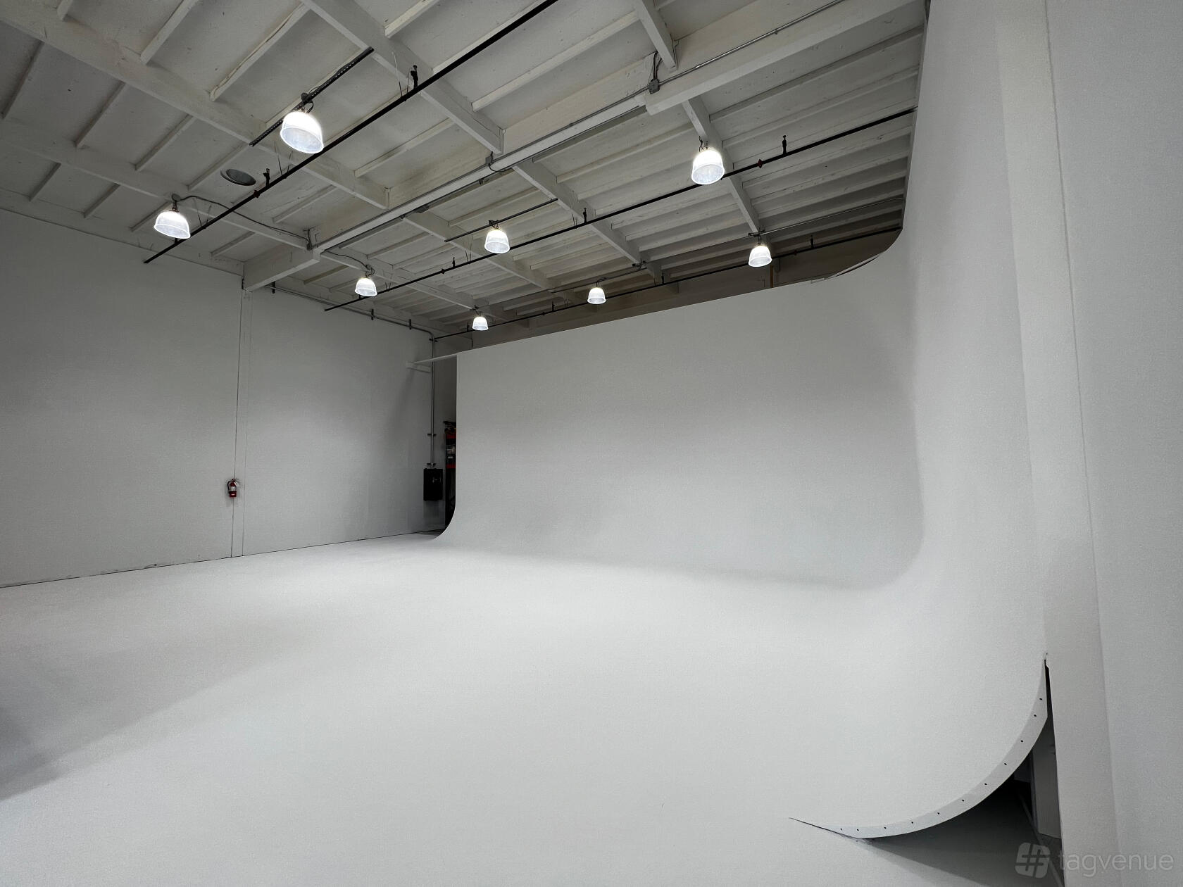 A photo studio with seamless white cyclorama walls, exposed ceiling beams, and overhead pendant lighting at StoodilyDoodleyO.