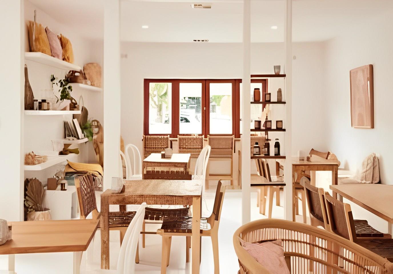 A cafe with natural wood tables, wicker chairs, and white walls with shelves at Lennox Cafe.