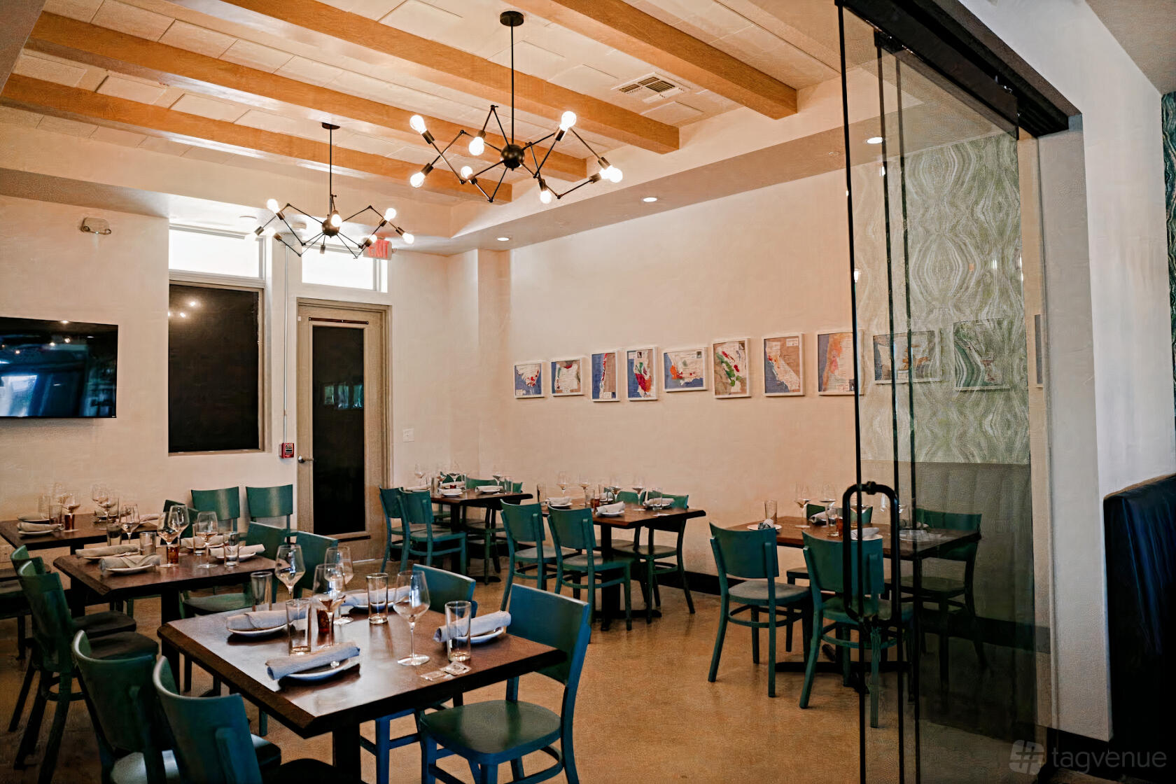 A dining room with teal chairs, set tables, framed artwork, and modern chandeliers at Clink Wine Bar & Bites.