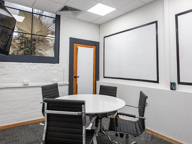 A meeting room with a round white table, black chairs, large whiteboards, and a TV at Engine Room St Kilda.