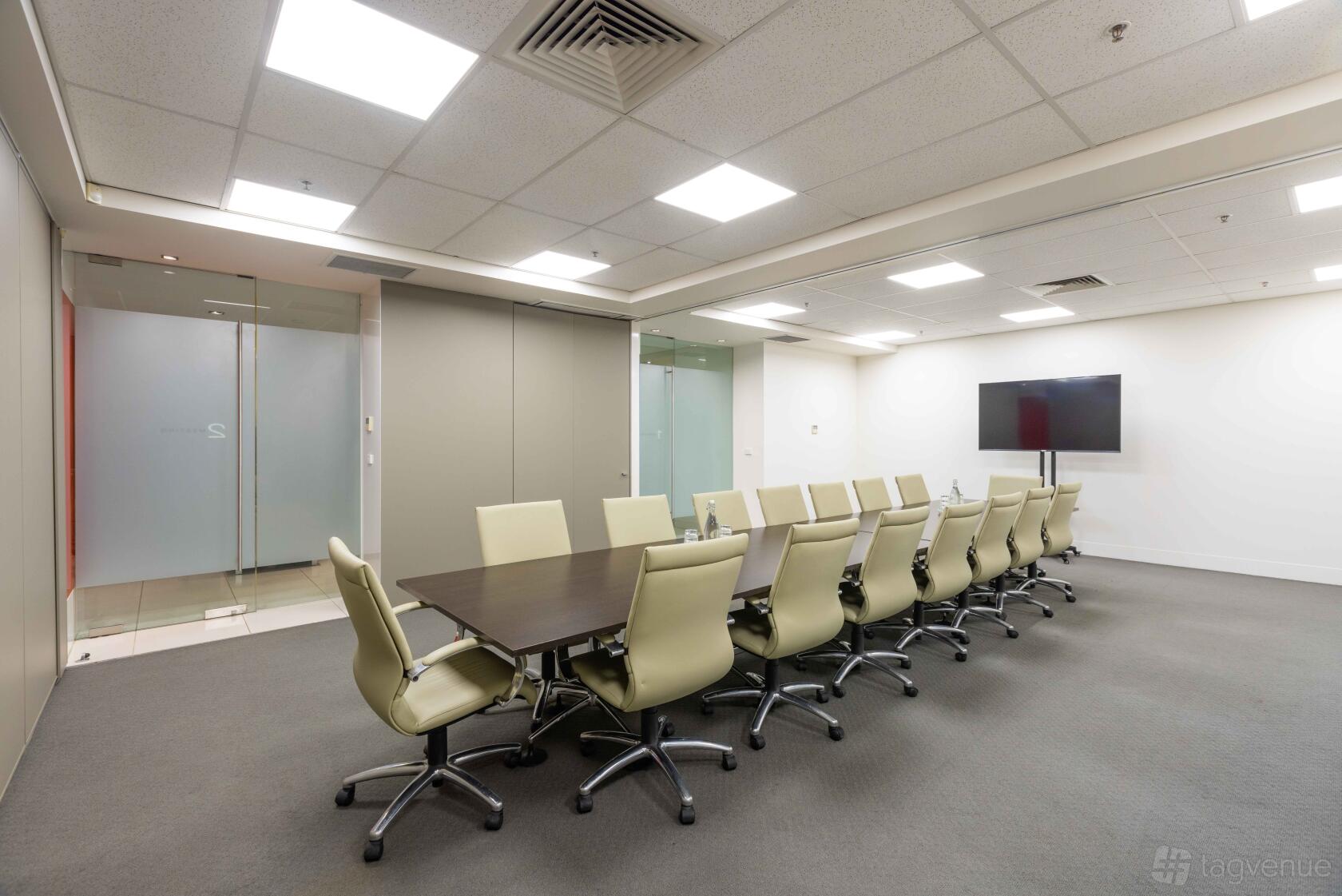 A boardroom with a long conference table, cream swivel chairs, and a wall-mounted screen at Business Centre @ 365.