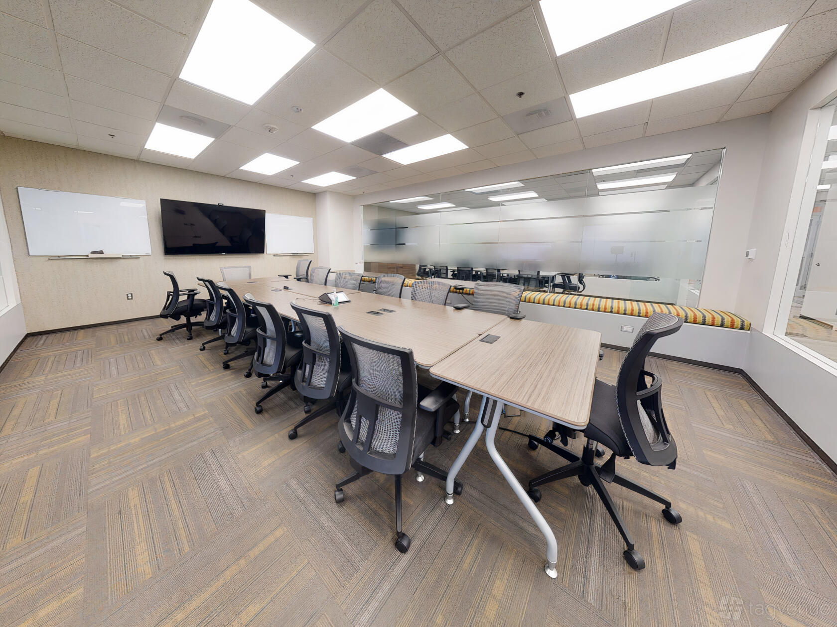 A boardroom with a long conference table, ergonomic chairs, glass wall, and large monitor at Launch Workplaces - Rockville.