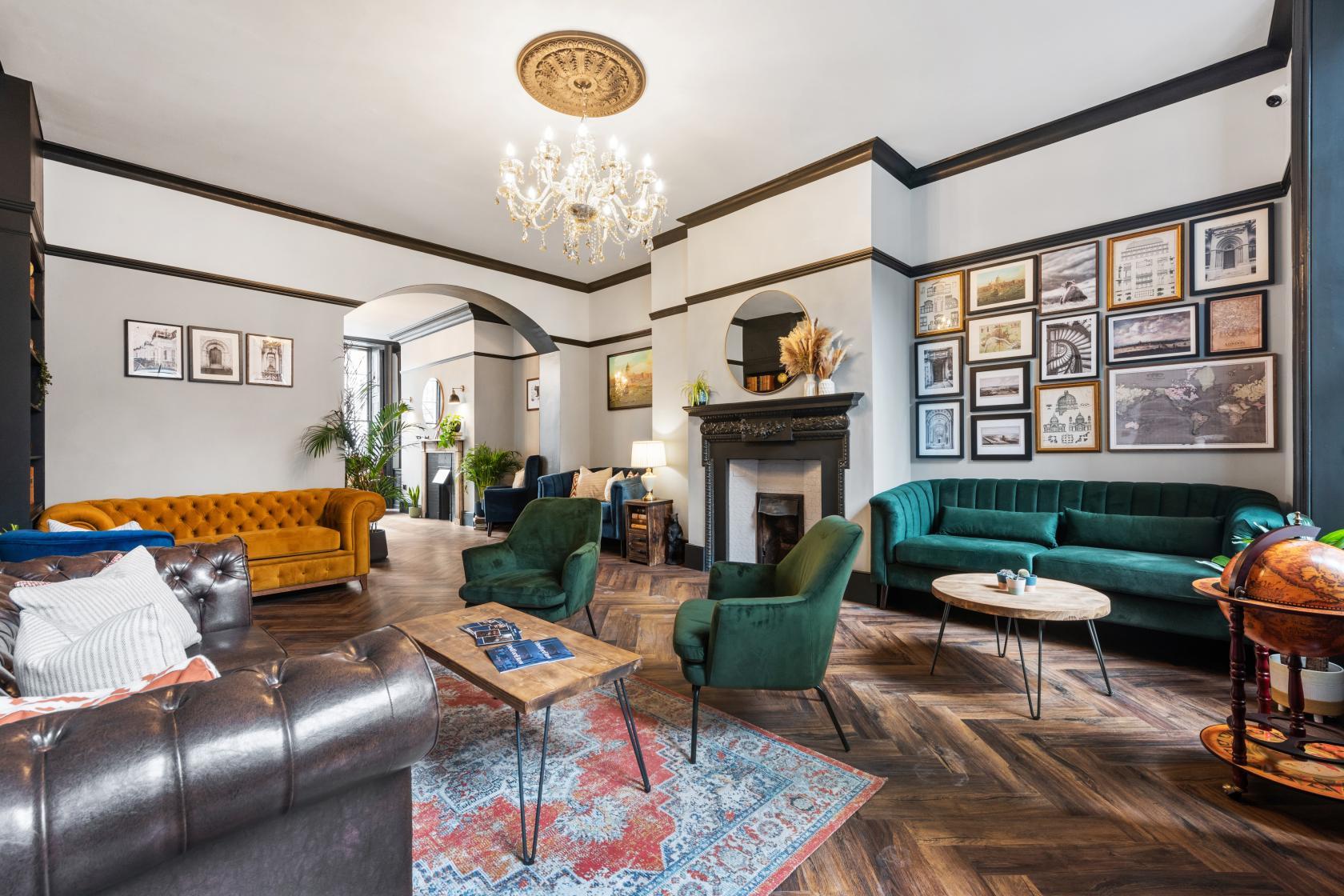 A coworking space with velvet sofas, a chandelier, framed artwork, and a fireplace at Bedford Row House.