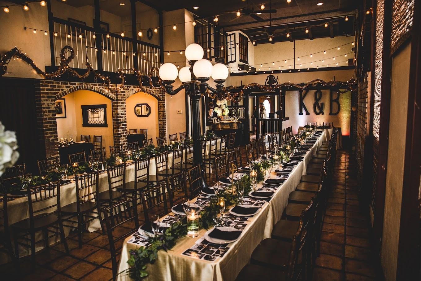 An event venue with long banquet tables, candle centerpieces, string lights, and exposed brick at Country Garden Caterers.