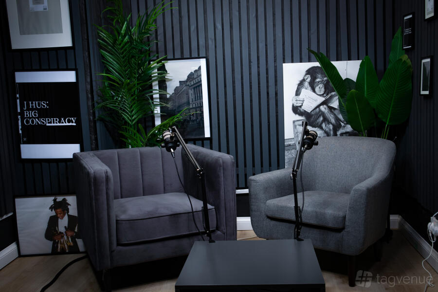 AB Studio podcast room with two grey chairs, boom microphones and a black acoustic slat wall