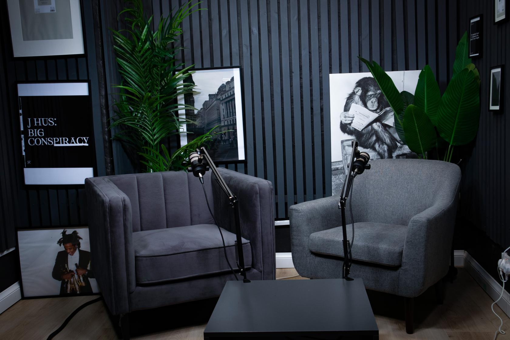 A recording studio with two armchairs, microphone stands, framed wall art, and potted plants at AB Studio.