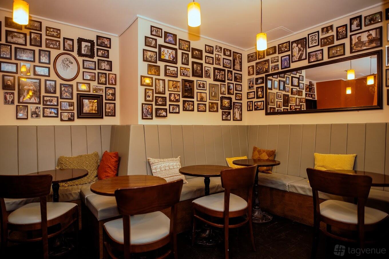 An event space in a bar with cushioned corner sofas, round wooden tables, and walls covered in framed photos at Fam Bar.