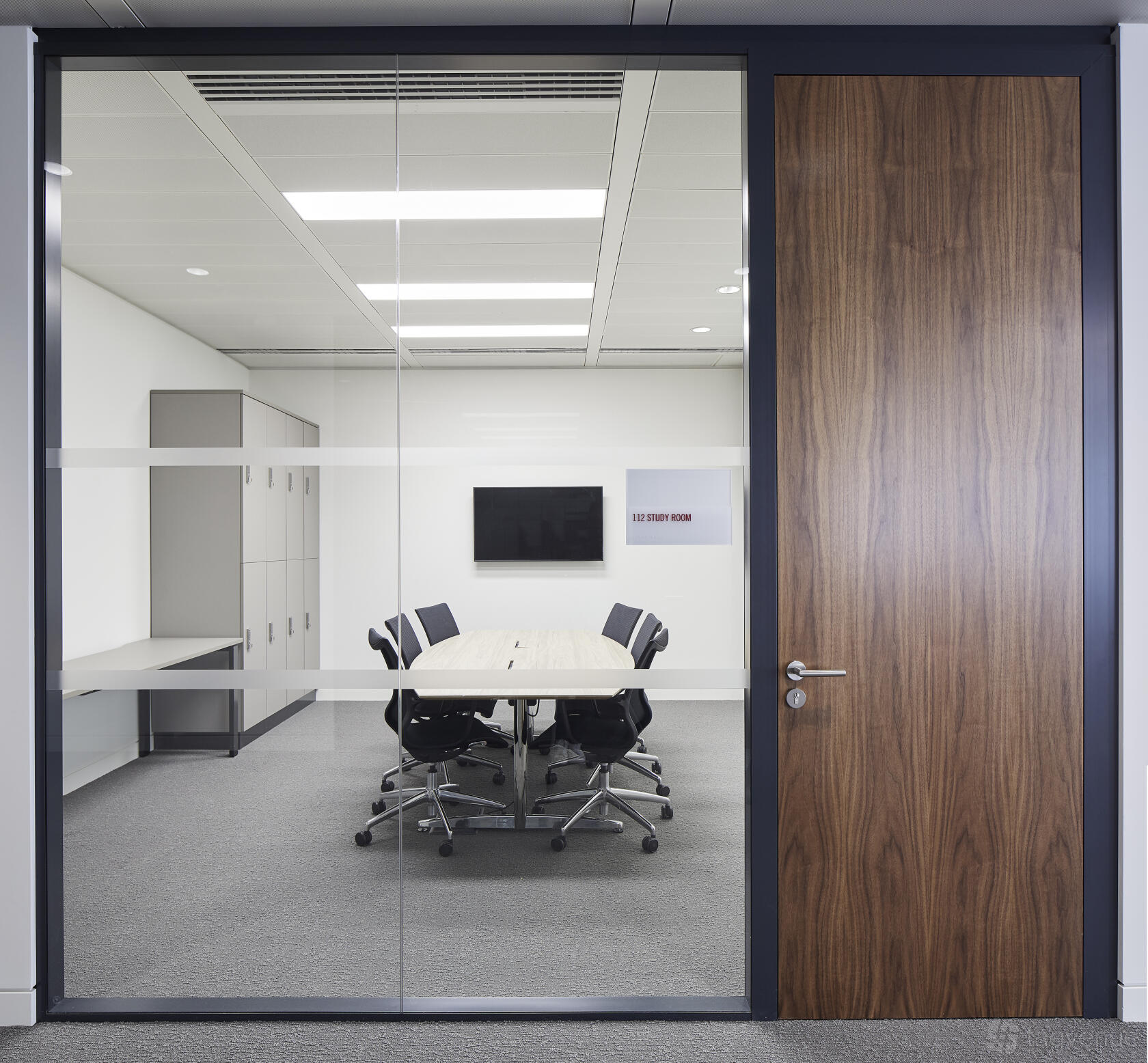 A meeting room with a long oval table, black office chairs, a wall-mounted TV, and glass walls at London Conference Centre.