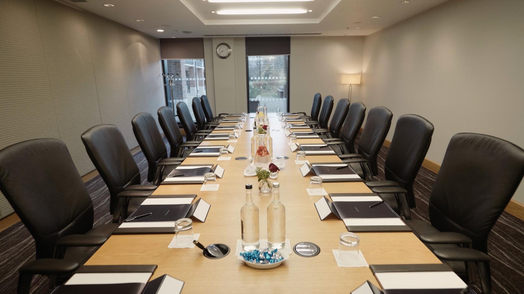 A hotel meeting room with a long boardroom table, executive chairs, notepads, and bottled water at Hilton London Heathrow Airport Terminal 5.