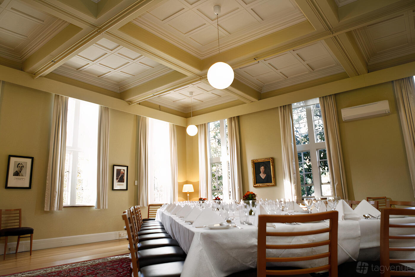An event space with high coffered ceilings, large curtained windows, and a long table set for dining at University College.