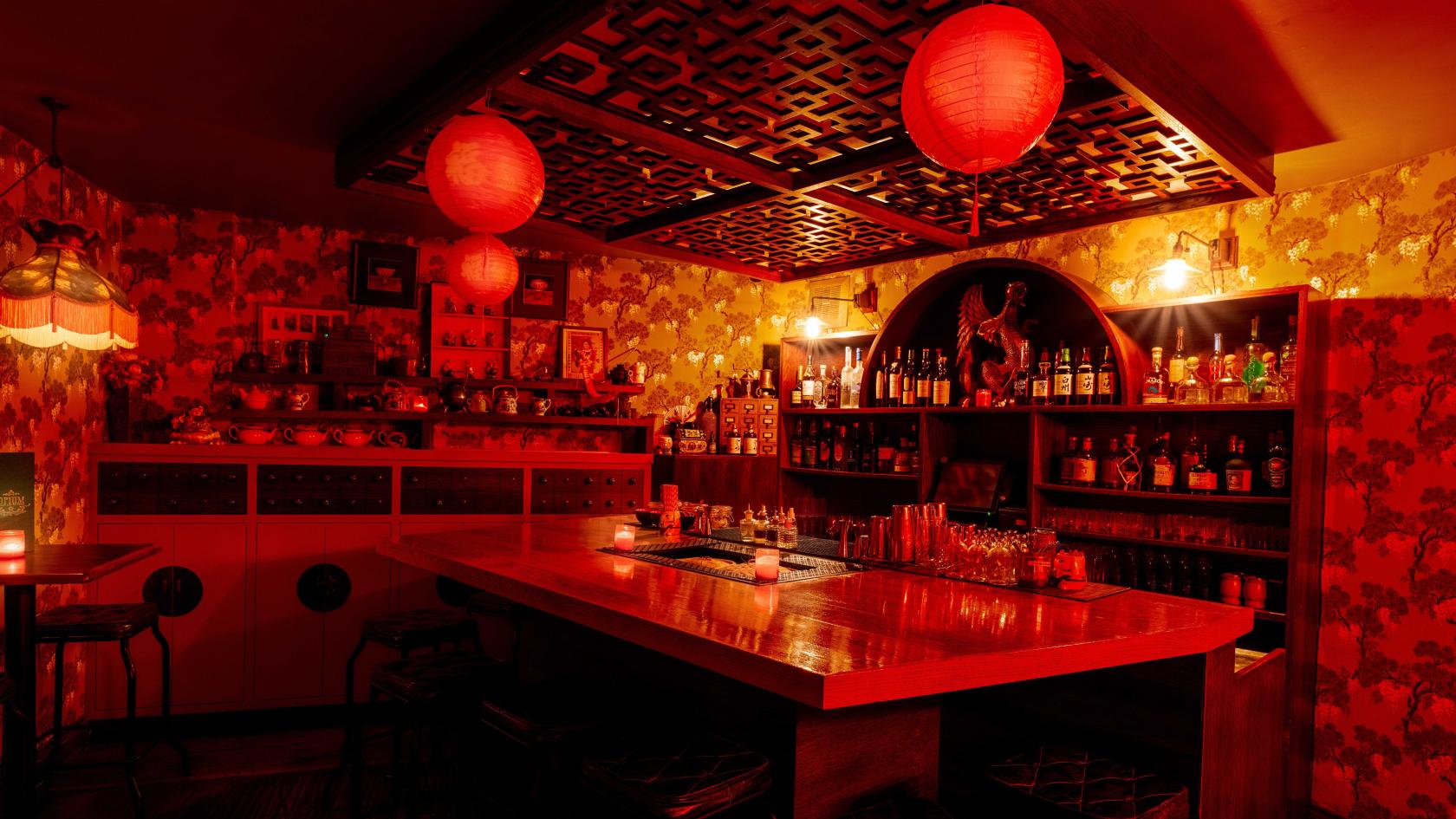 An event space in a cocktail bar with red lanterns, patterned ceiling panels, and a stocked wooden bar at Opium Cocktail & Dim Sum Parlour.