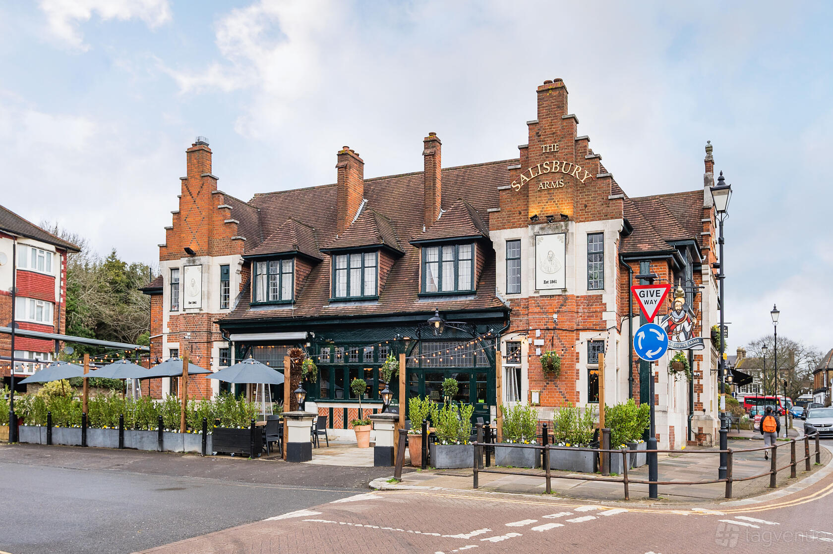 A traditional brick pub with gabled roof, outdoor seating area, and umbrellas at The Salisbury Arms Winchmore Hill.