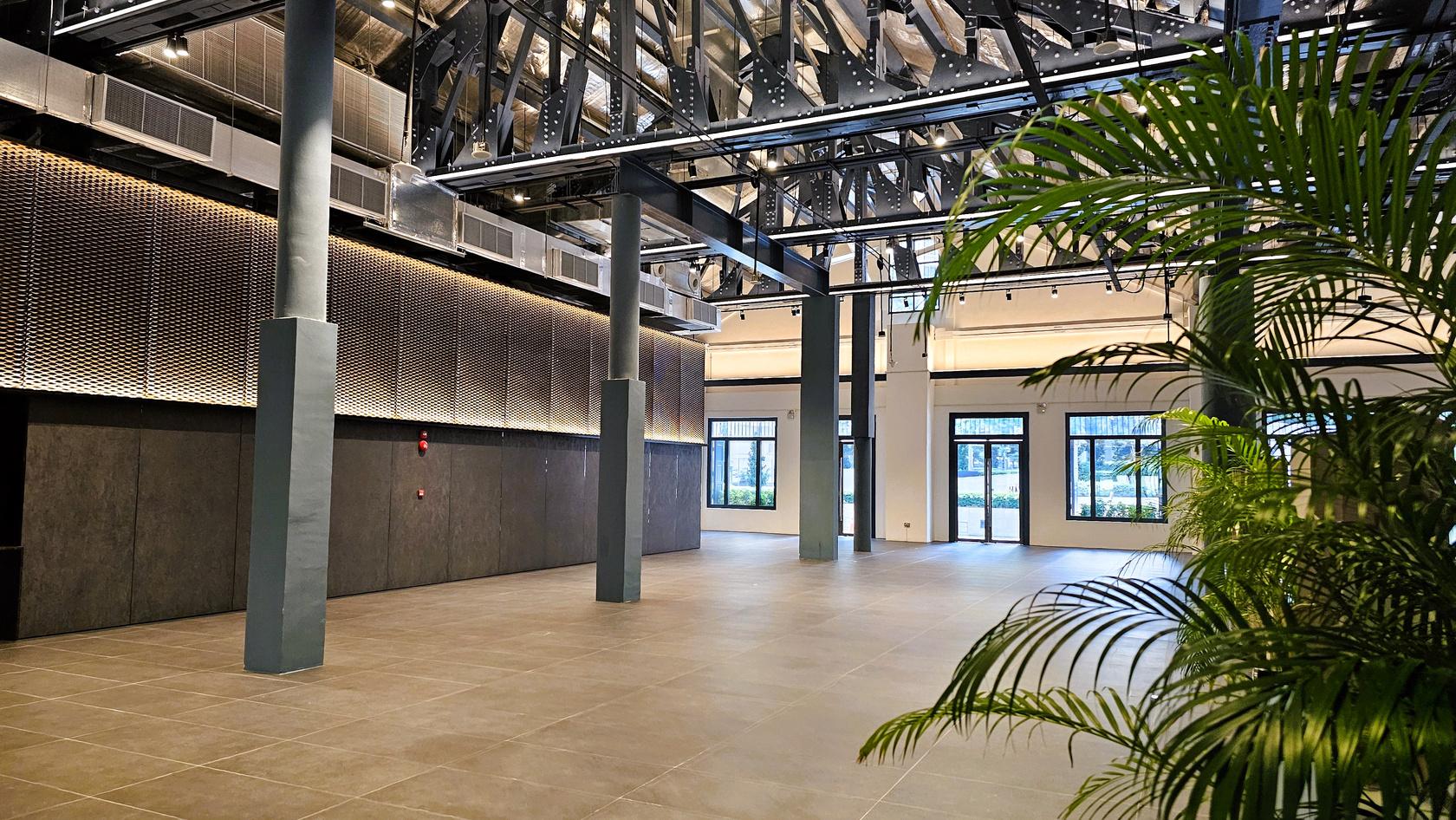 A warehouse with high exposed beam ceilings, large windows, and tiled flooring at Warehouse @ River Promenade.