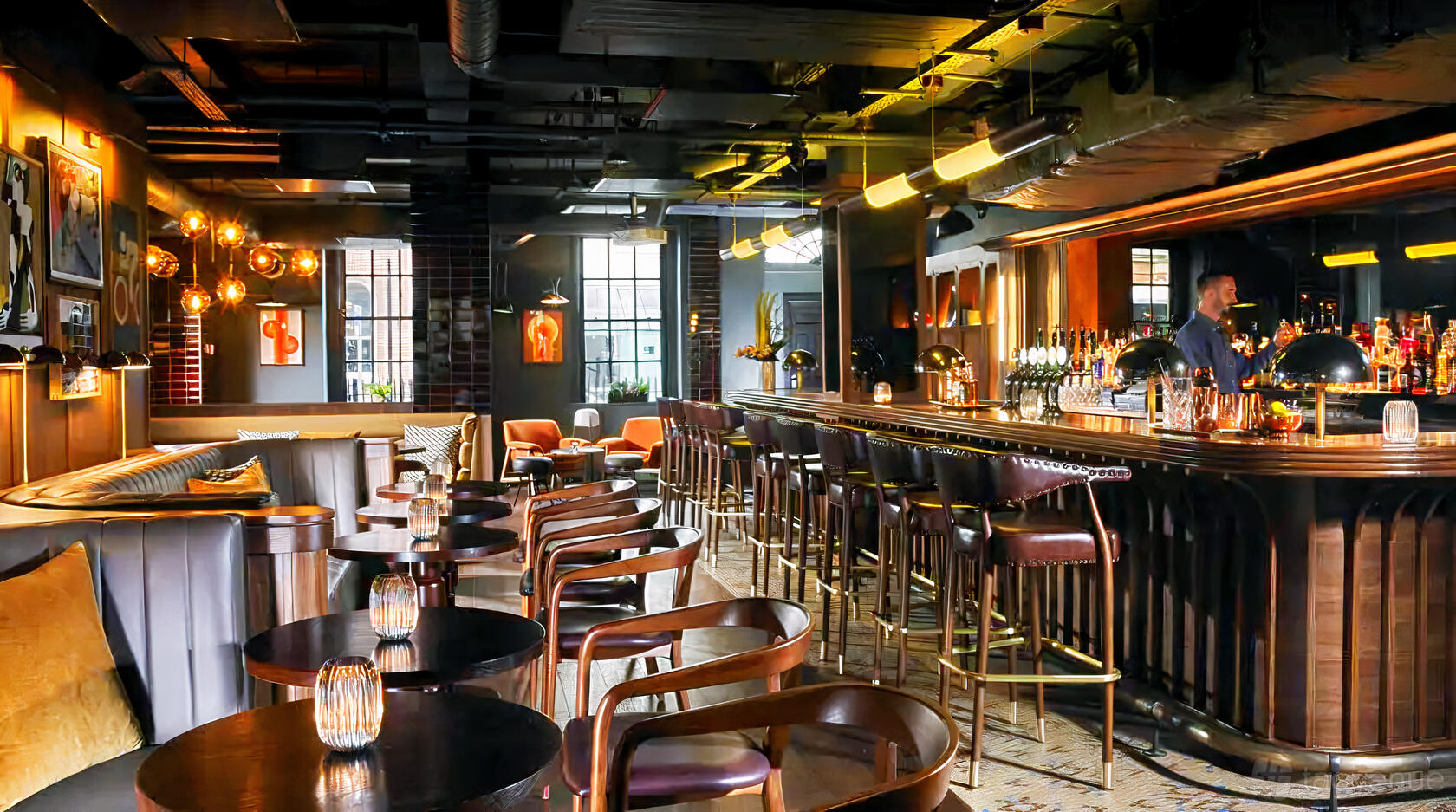 A hotel bar with leather seating, round wooden tables, pendant lighting, and a long bar counter at The Mont.