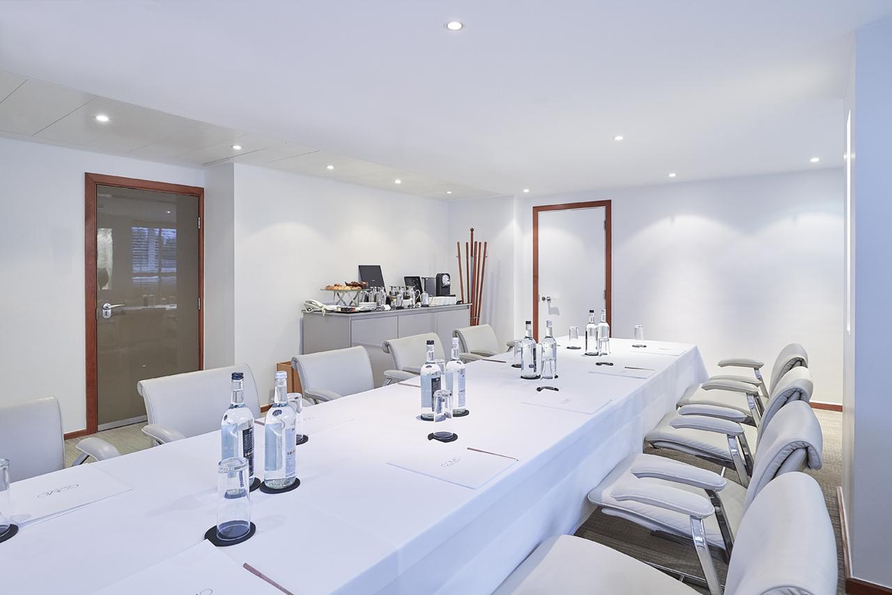 A hotel boardroom with a long white-clothed table, cream chairs, and bottled water at COMO Metropolitan London.