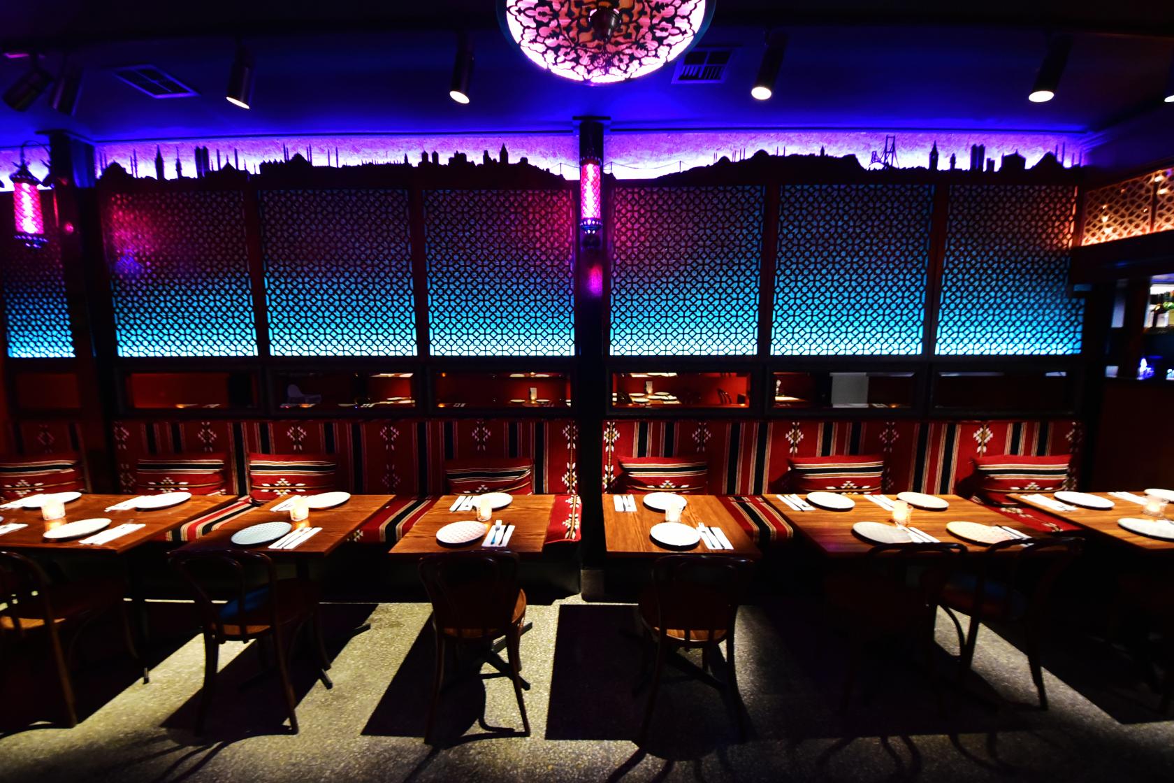 A restaurant with patterned lattice walls, colorful uplighting, and long wooden tables set for dining at Marmara Restaurant.