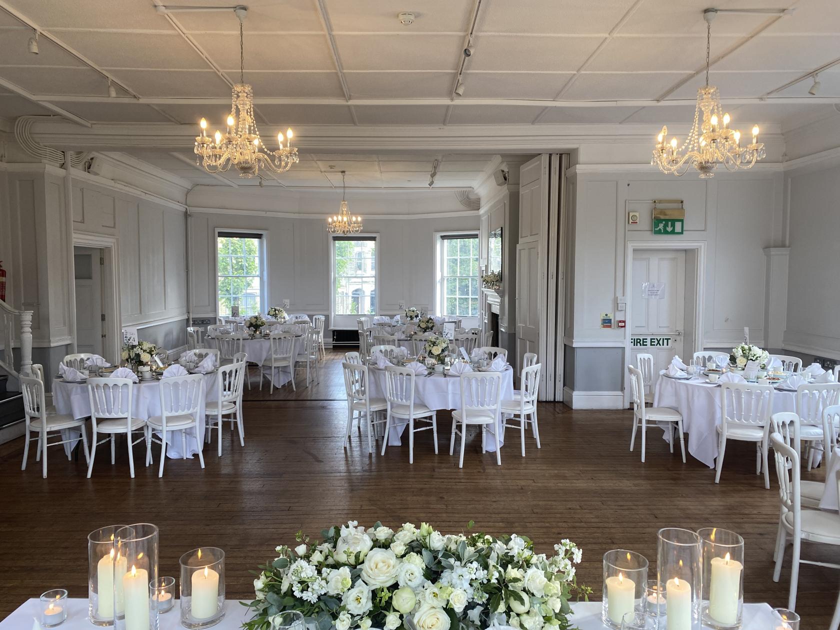 An event venue with chandeliers, large windows, and round tables with white linens at Winchester House.