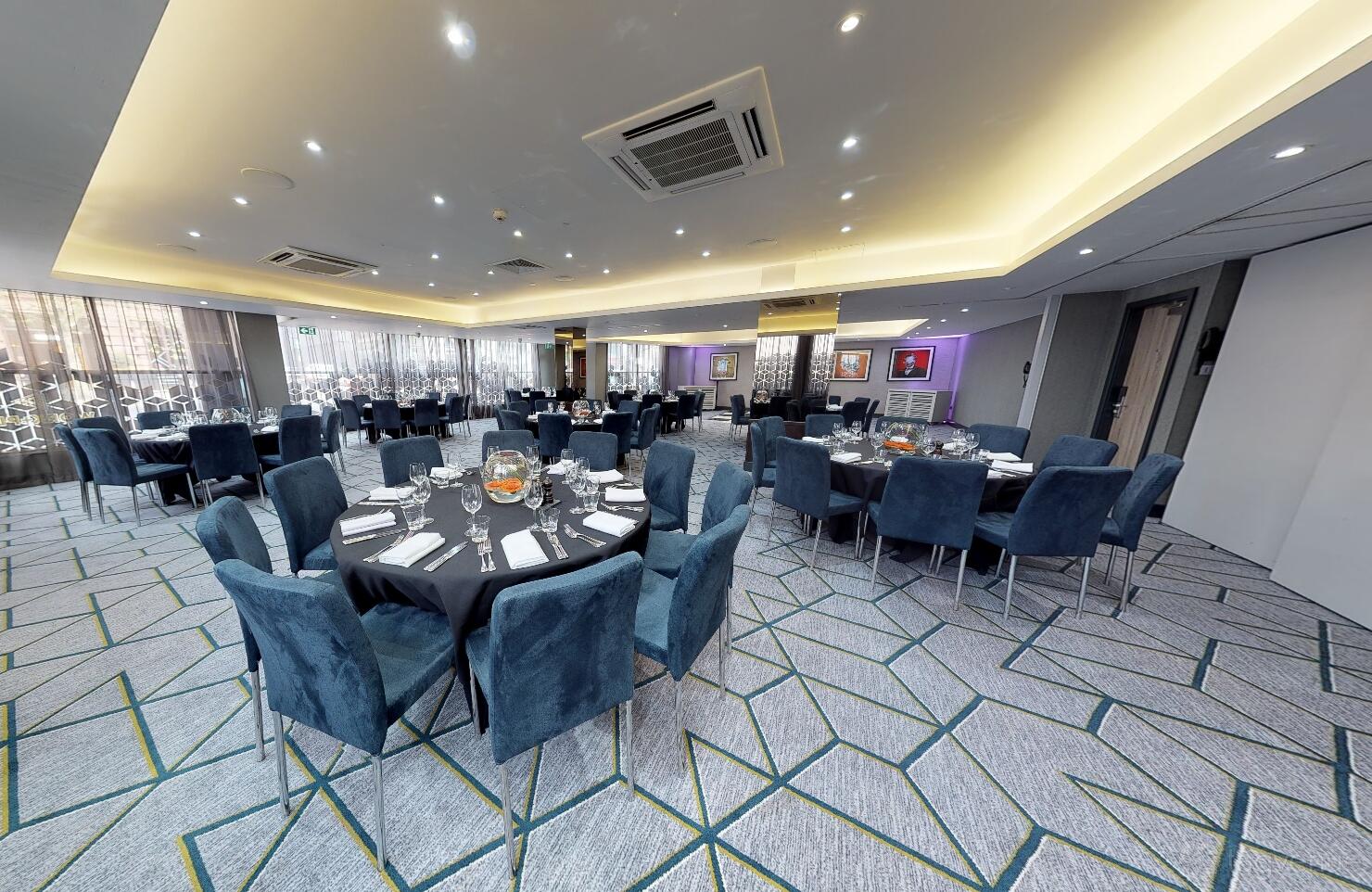 A function room with round tables draped in black linens, blue velvet chairs, and geometric carpet at Malmaison Manchester.