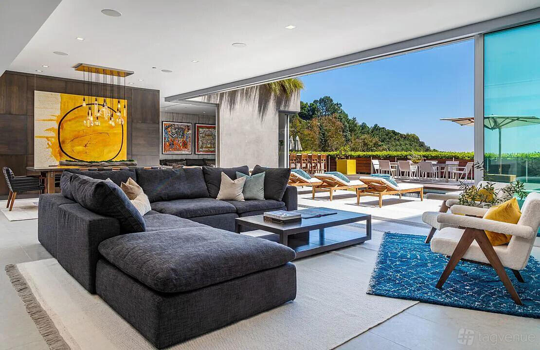An apartment with a spacious lounge, gray sectional sofa, floor-to-ceiling windows, and outdoor patio at Luxury Villa Above Sunset Strip.