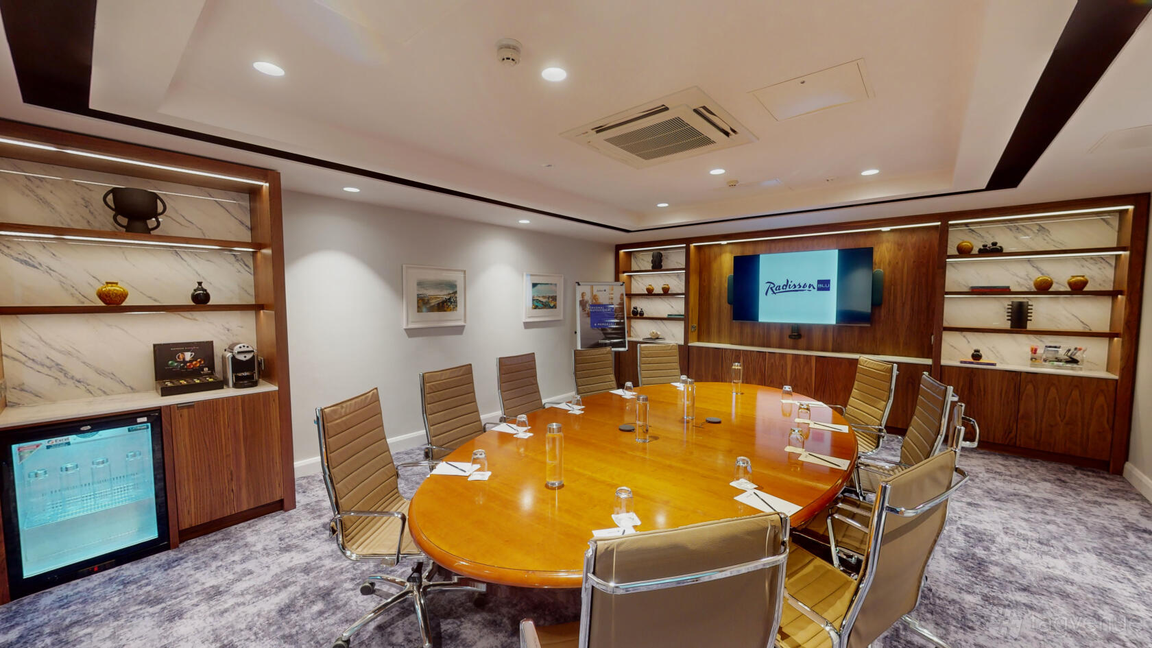 A meeting room with an oval wooden table, leather chairs, wall shelving, and a screen at Radisson Blu Hotel, Dublin Airport.