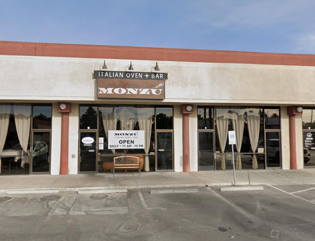 A restaurant exterior with large windows, beige curtains, and a sign reading 'Monzú Italian Oven + Bar'.