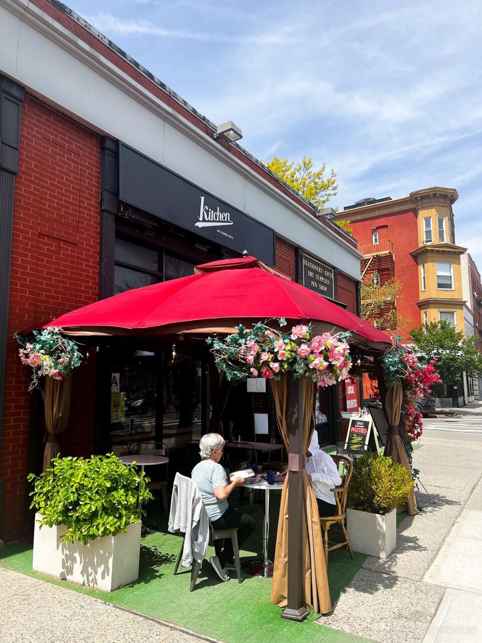 An outdoor restaurant patio with a red canopy and floral decorations at Kitchen at Cobble Hill.