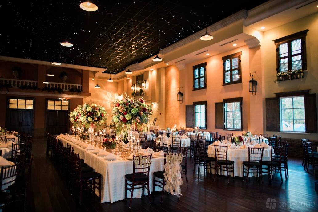 An event venue with long banquet tables, elegant floral centerpieces, wooden chairs, and a ceiling with twinkling lights at The Villa Tyler.