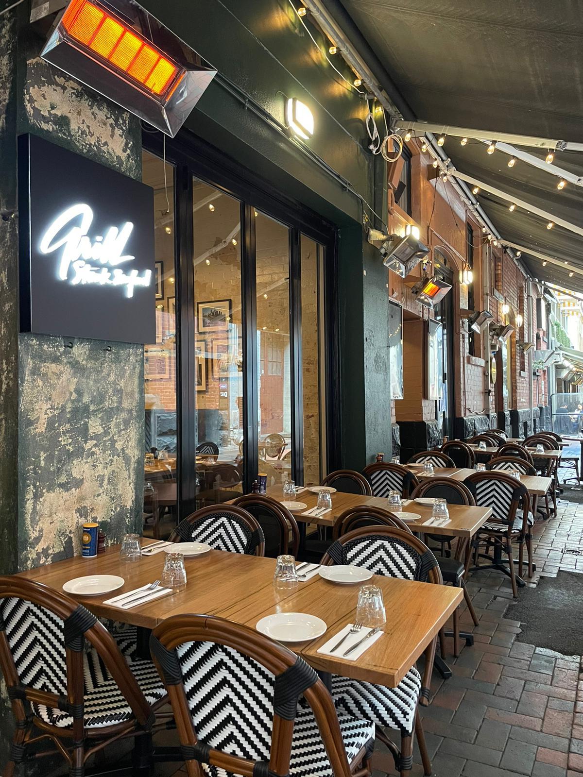 An outdoor dining area with woven chairs, set tables, and string lighting at Grill Steak Seafood