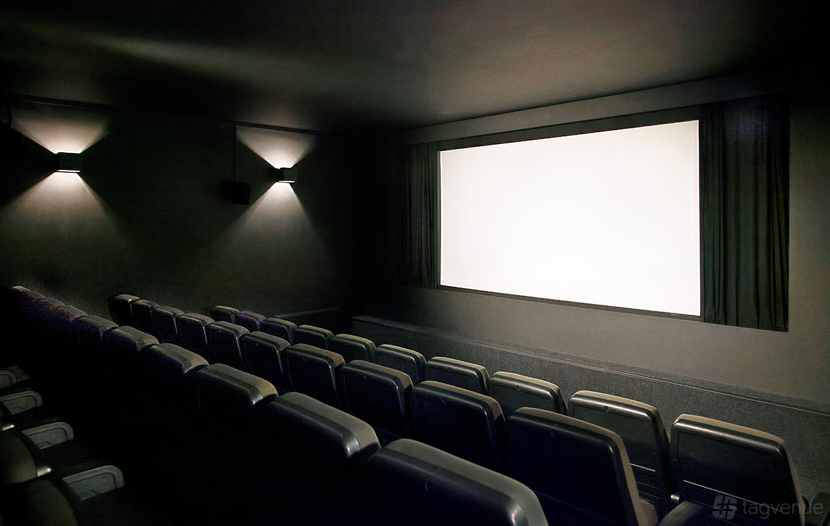 A cinema with tiered seating, wall-mounted lights, and a large projector screen at Close-Up Cinema.