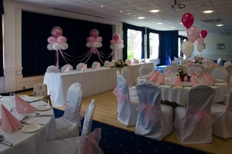 An event space with round tables draped in white linens, pink napkins, and balloon centerpieces at Sindlesham Court.