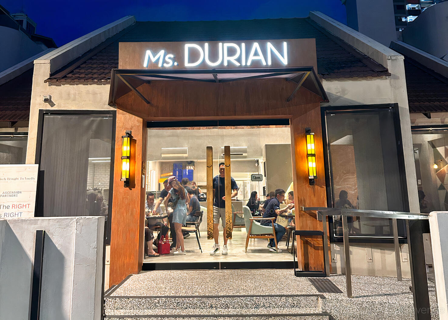 A café with large glass doors, warm lighting, and visible patrons inside at Ms.Durian.