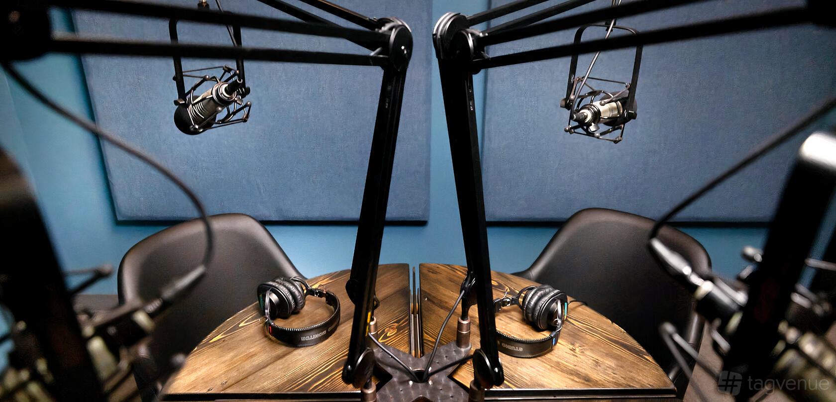 A podcast studio with mounted microphones, acoustic panels, and headphones on a round wooden table at MCM Stages.
