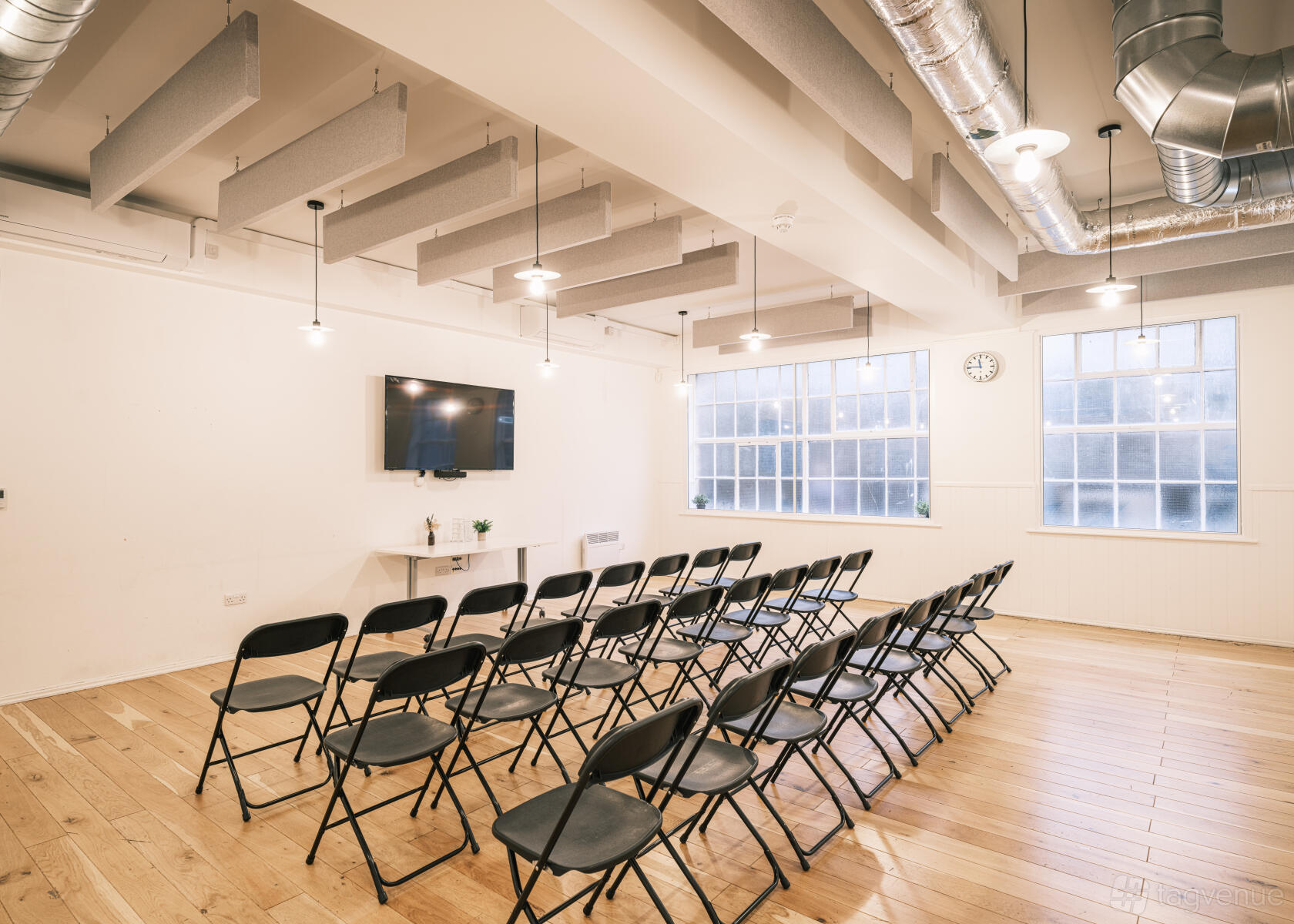 An event space with rows of black chairs, wooden flooring, large windows, and wall-mounted TV at King's House.