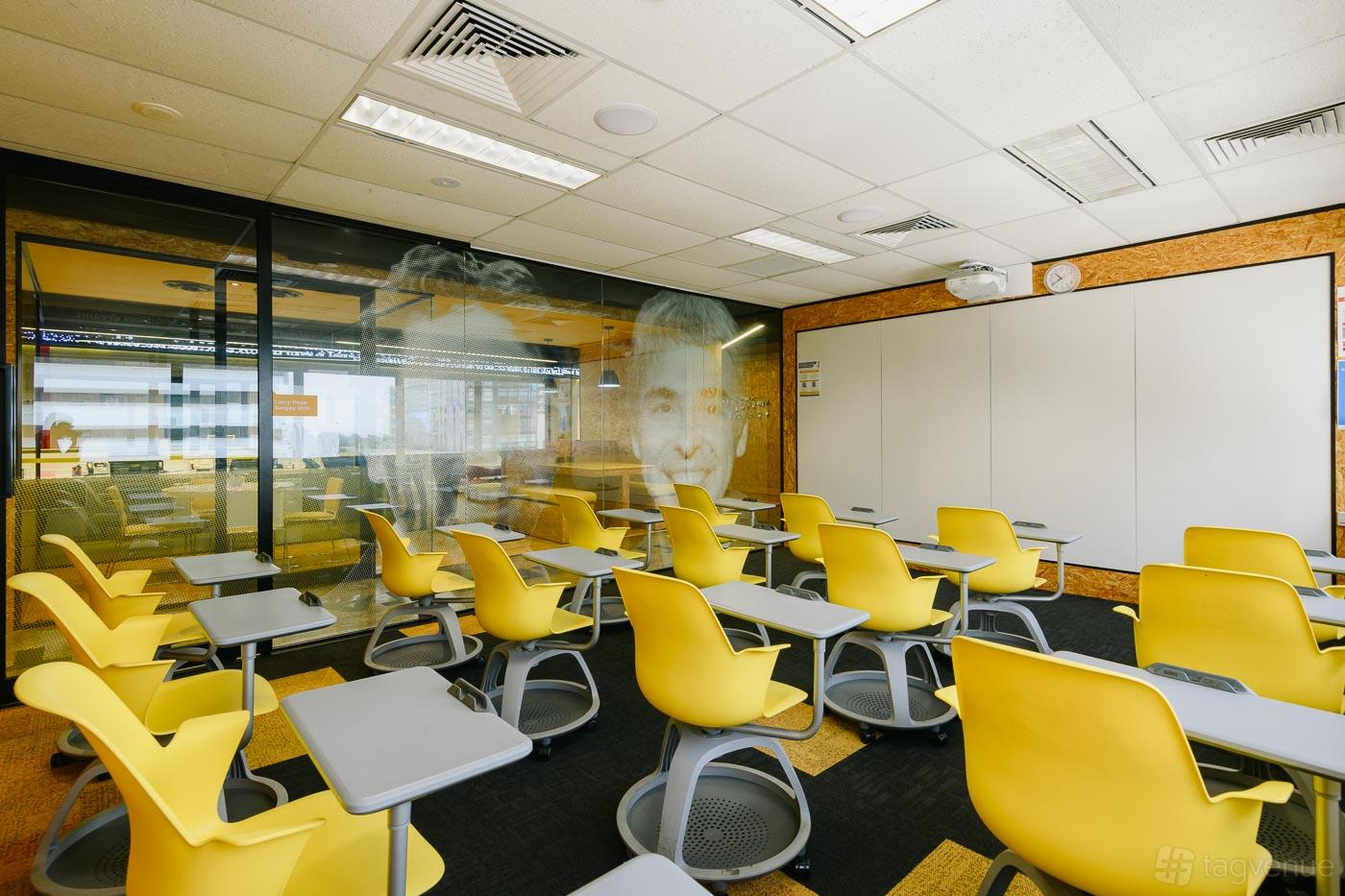 A classroom with yellow swivel desks, individual tablet arms, and glass walls at Chatswood Learning Centre.