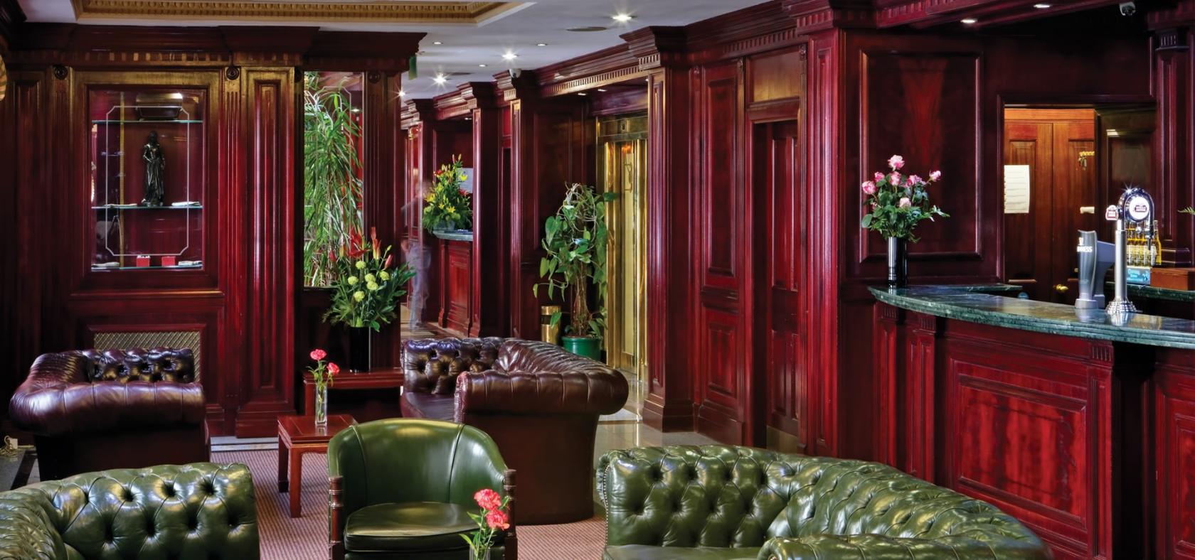 A hotel lounge with deep red wood paneling, leather armchairs, and floral arrangements at Fitzrovia Hotel.