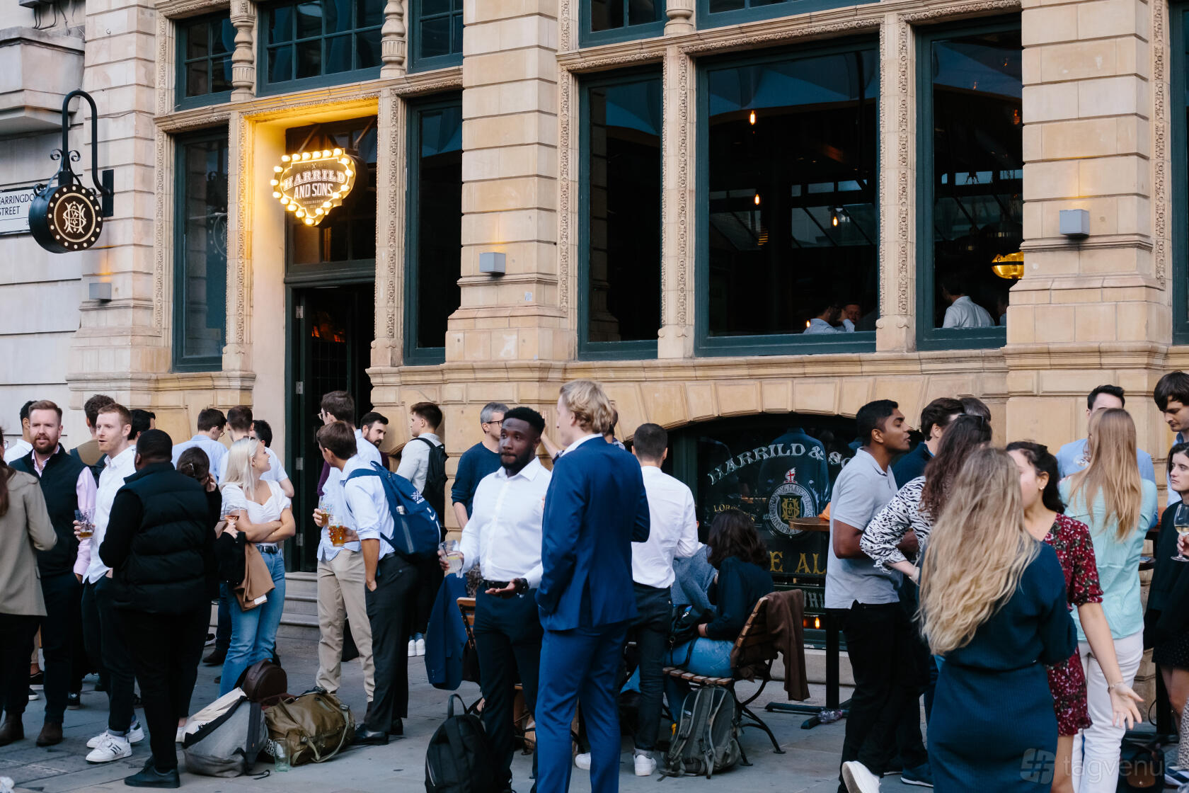 A restaurant with people gathered outside a stone facade with large windows at Harrild & Sons.